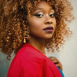 Striking portrait of a woman with curly hair, wearing a red jacket.